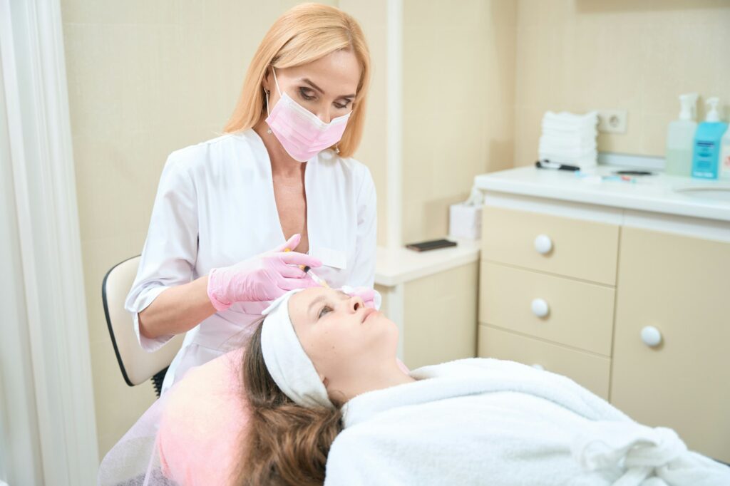 Female cosmetologist in mask makes injection to client. Acne treatment